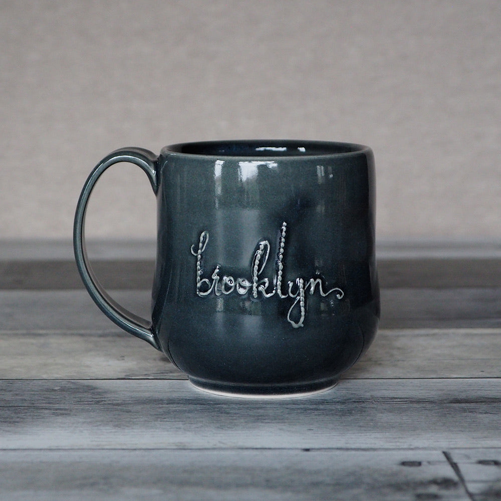 A gray curved mug with the word Brooklyn in script.