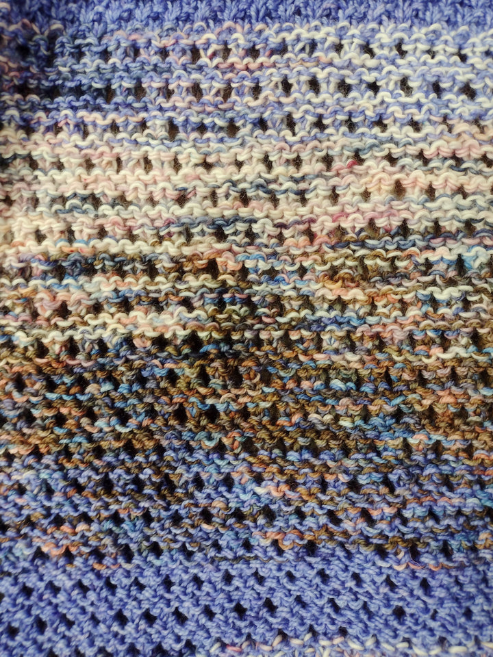 A close-up of a textured and eyelet knit fabric in pink, blue, blue-purple and brown. 