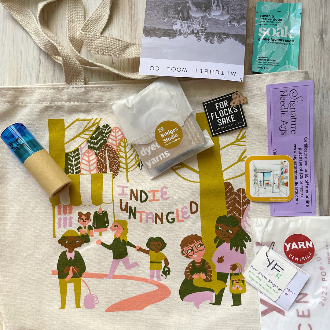 : A cotton tote bag with an illustration of a diverse group enjoying a yarn festival.