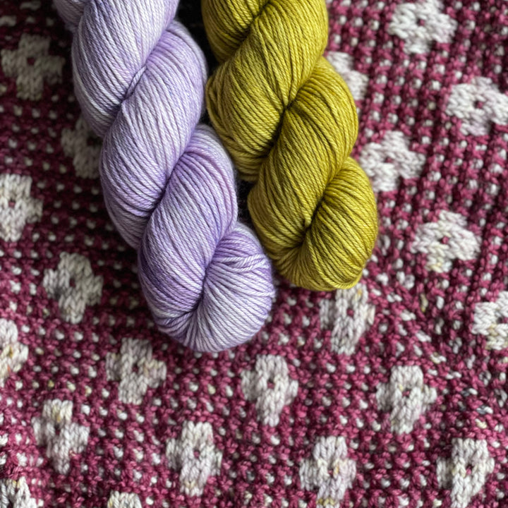 Lilac and green yarn above a gray and purple floral knit piece.
