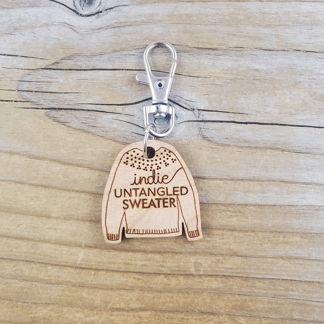 A wooden fob in the shape of a sweater and the words Indie Untangled Sweater.