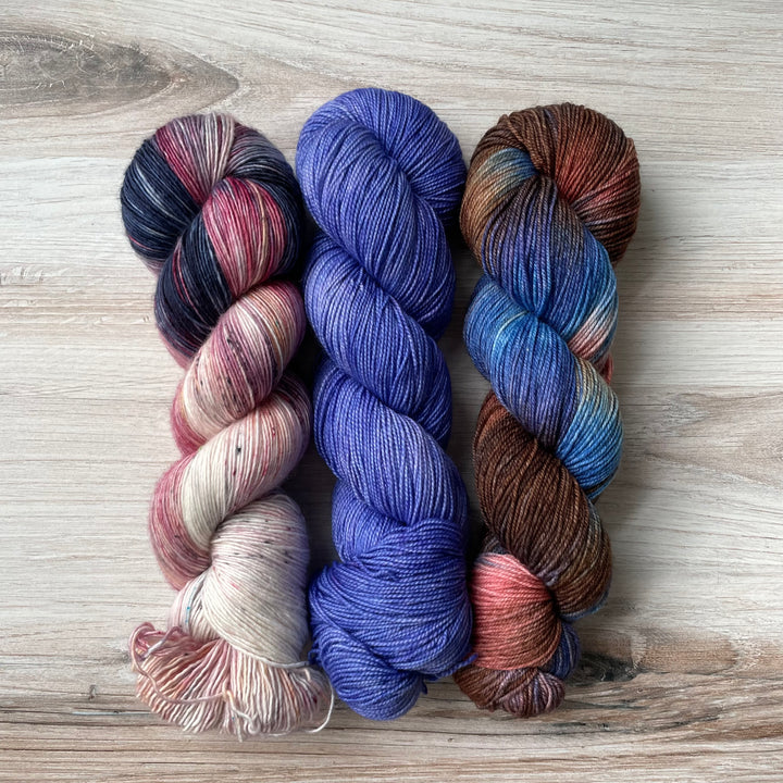 Three skeins of yarn in pink and blue speckle, solid blue-purple and variegated blue, brown and pink. 