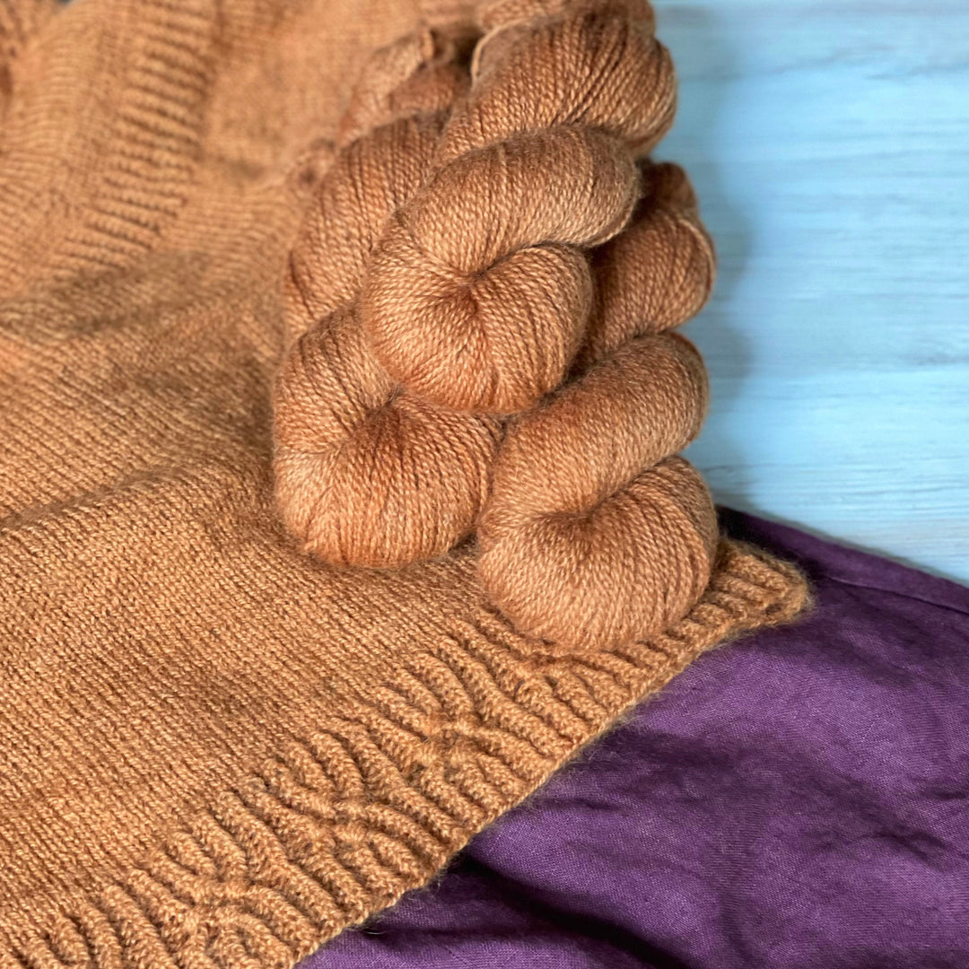 Orange yarn and an orange knit sweater laid out over a dark purple linen skirt.