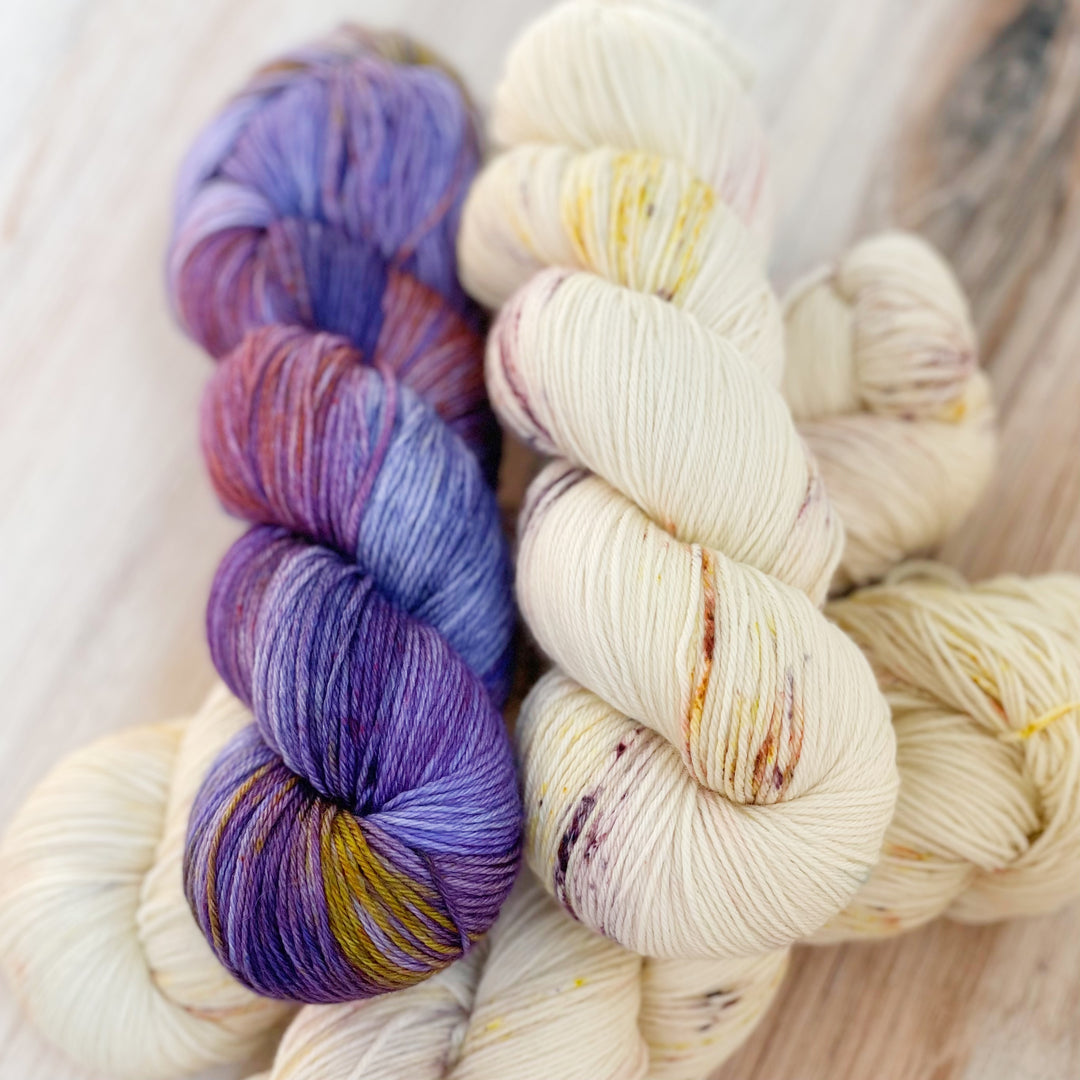 Twisted skeins of purple and cream-colored tarn with purple and gold speckles. 