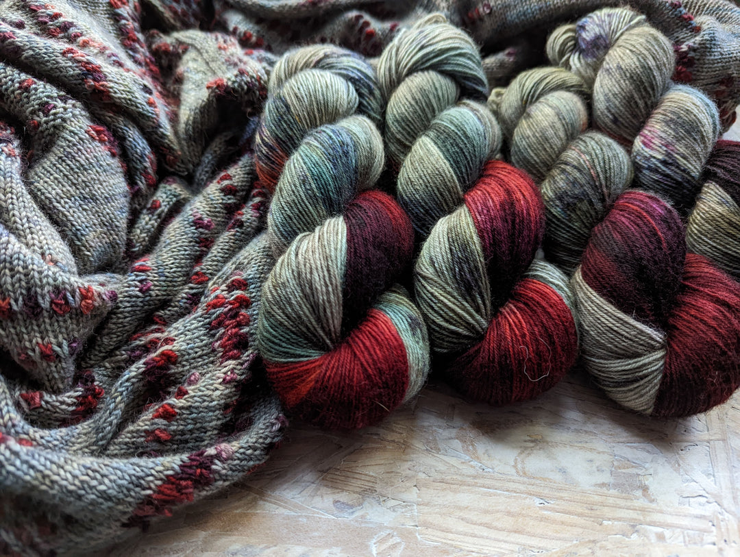 Gray-blue yarn and knitting with bands of red and purple.