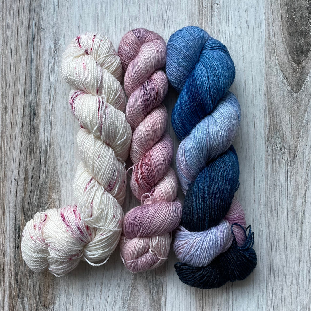 Three skeins of yarn in white with pink speckles, solid pink with faint pink speckles and variegated blue and pink