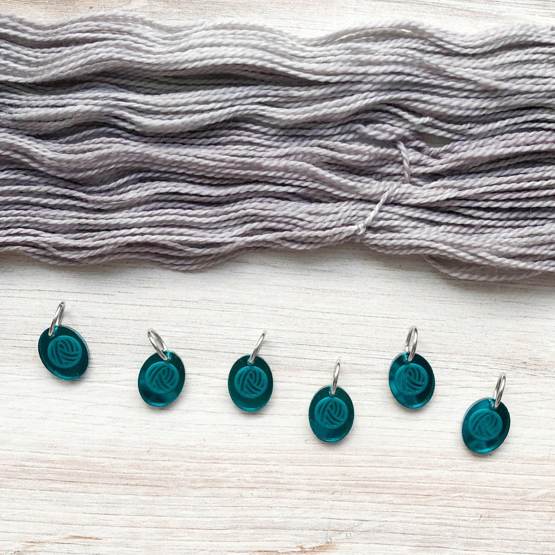 Teal acrylic stitch markers with a yarn ball image below a loose skein of gray yarn.