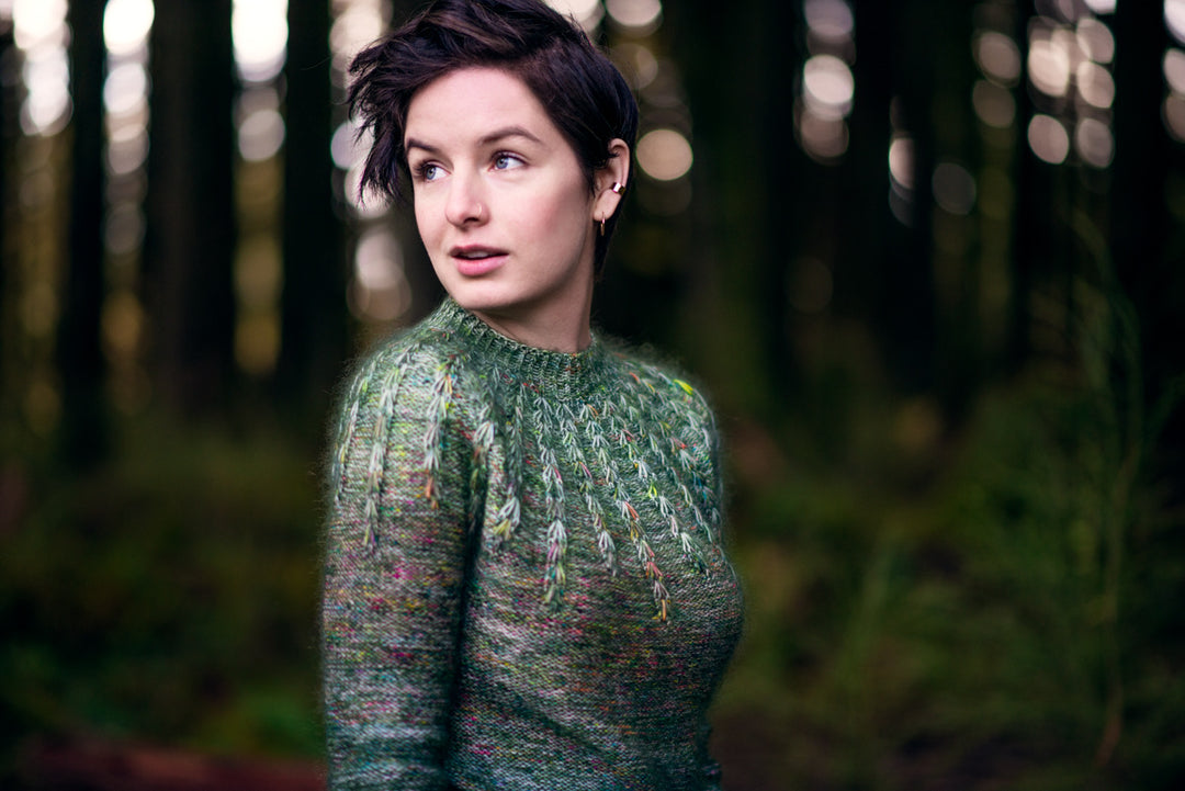 A white woman in a green speckled ombre sweater.