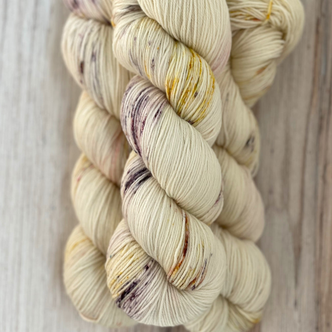 Twisted skeins of cream-colored tarn with purple and gold speckles. 
