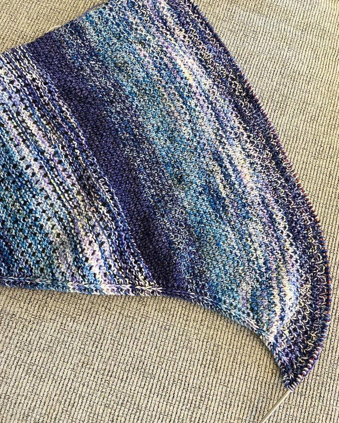 A textured and eyelet shawl with fringe in blue, purple, pink, yellow and white yarn faded together. 